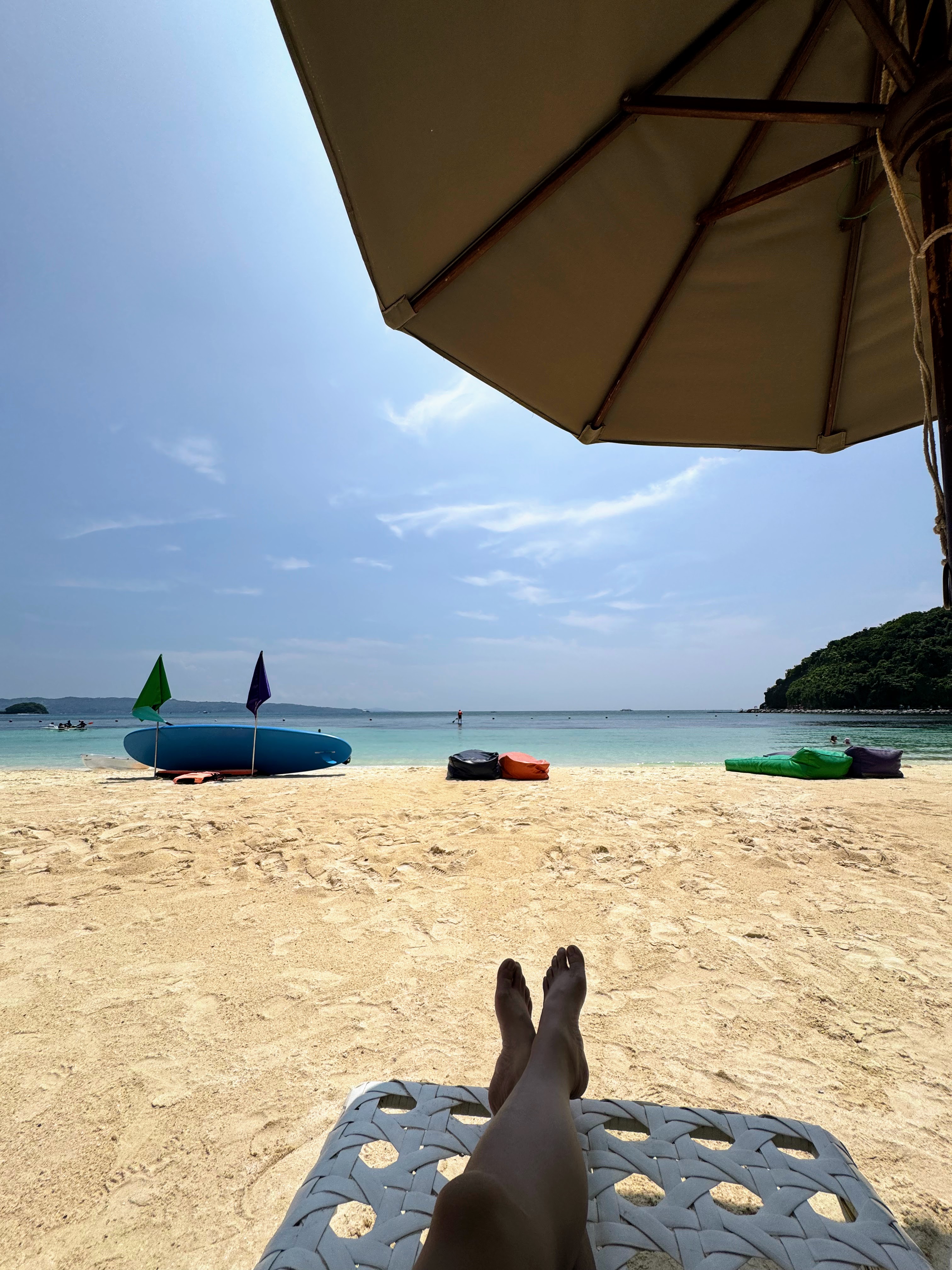 A shaded beach view with turquoise water and boats on the sand