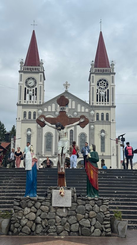 Front view of Baguio Cathedral with its twin red spires and a crucifix in the foreground.