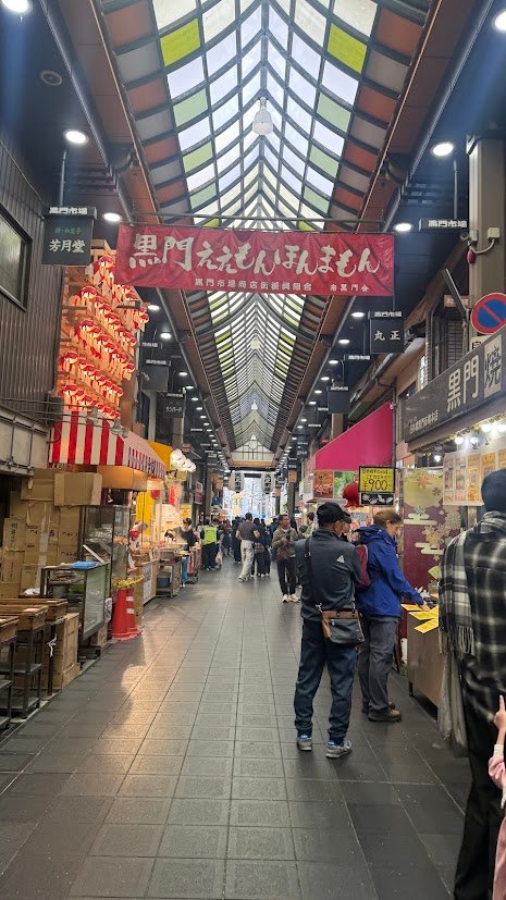 Covered market street lined with food stalls and visitors at Kuromon Ichiba Market.