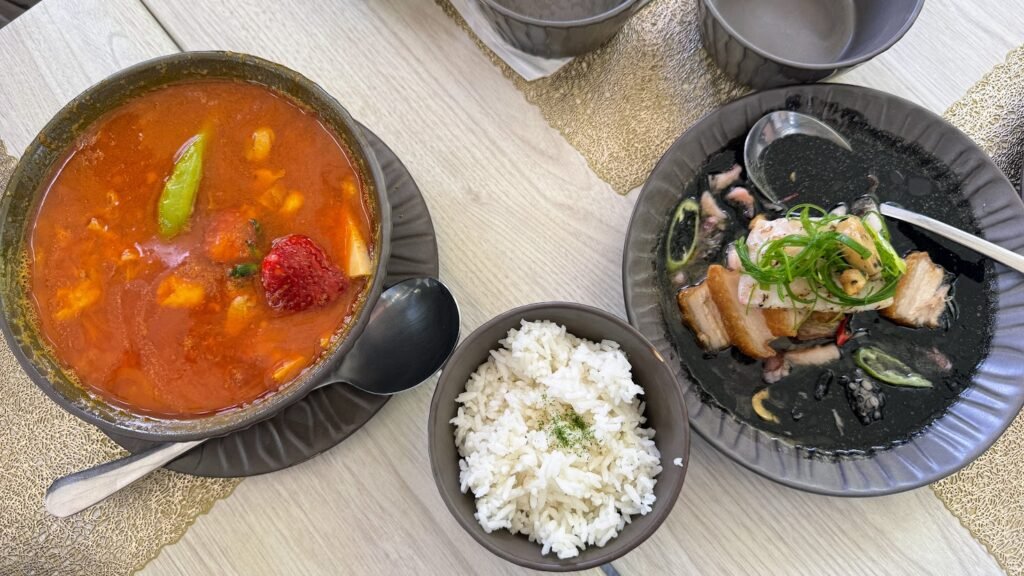 Bowl of Strawberry Sinigang served with rice and a black seafood dish.